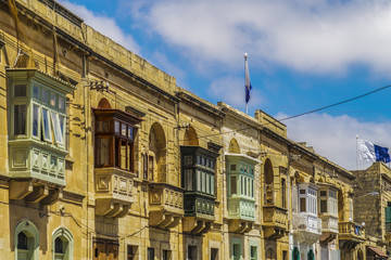 Fototapeta premium Gozo, Malta traditional buildings with colored balconies. Day view of Maltese limestone buildings at Triq Sant Orsola street Victoria Town, Malta.