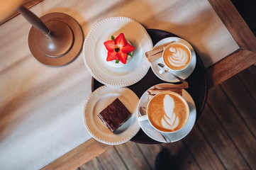 Coffee house. Two cups on a wooden table. Coffee for a couple. Dessert. Brownie, cheesecake. Cappuccino, latte, foam.