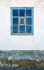 Iconic blue wooden window on white stone wall of typical rural abandoned house