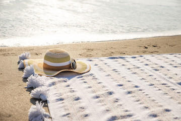 Hat on a blanket on sandy beach with ocean wave in background