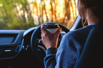 A young woman drinks coffee while driving a car while traveling. The concept of traffic safety
