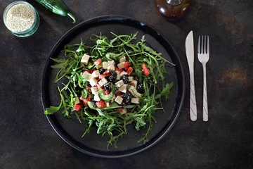 Wandaufkleber Gesunder Salat. Grüner Salat auf Rucola, Wassermelone, Tofu, schwarze Oliven serviert auf einem schwarzen Teller © Robert Przybysz