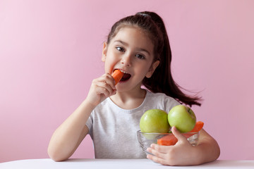 A cute little girl eating fresh vegetables. A portrait on pastel background. Healthy teeth.