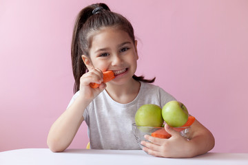 A cute little girl eating fresh vegetables. A portrait on pastel background. Healthy teeth.