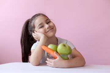 A cute little girl eating fresh vegetables. A portrait on ? pastel background. Healthy teeth.
