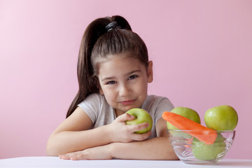 A cute little girl eating fresh vegetables. A portrait on ? pastel background. Healthy teeth.