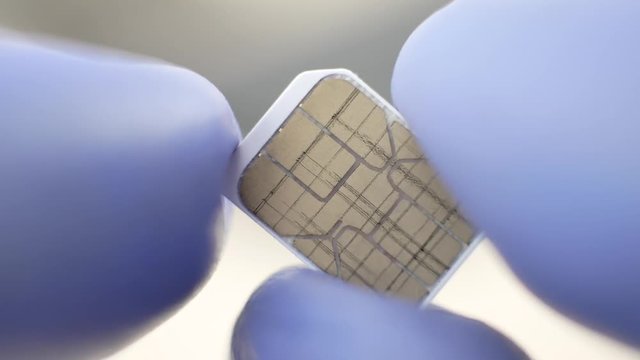 Communication equipment engineer in blue gloves holding micro SIM card at laboratory or factory