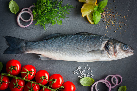 Raw seabass fish with ingredients for cooking a hot dish, top view