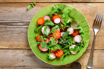 Vegetarian salad of arugula, tomato, radish and mozzarella cheese on an old wooden table.