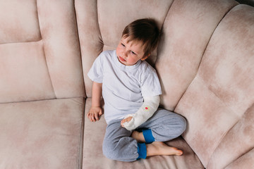 a small boy is sitting on a chair with a broken arm, in a cast. hospital. medicine. danger. pain. to break limbs. violence.