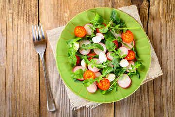 Vegetarian salad of arugula, tomato, radish and mozzarella cheese on an old wooden table.
