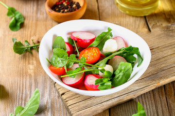 Vegetarian salad of arugula, tomato, radish and mozzarella cheese on an old wooden table.