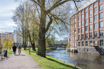 Unrecognizable people enjoy waterfront park Strömparken along Motala river in Norrkoping during spring in Sweden.