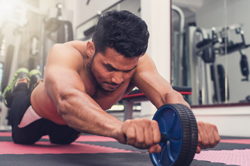Strong man bodybuilder  are exercising the abdomen with exercise wheel in Gym