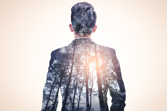 The double exposure image of the businessman standing during sunrise overlay with forest image. The concept of nature, freedom, environment and business.
