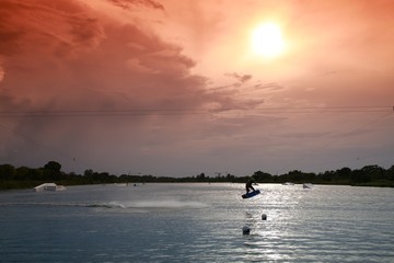 Wakeboarder Doing Half-Flip Being Pulled by Cable on Lake Against Late Afternoon Sun through Orange Graduated Filter