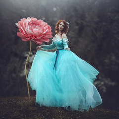 A beautiful sensual girl with red hair in a fairy-tale blue dress posing in the wind near a huge...