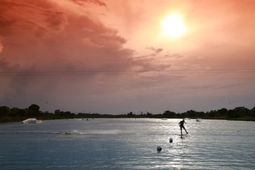Fototapeta premium Wakeboarder Doing Half-Flip Being Pulled by Cable on Lake Against Late Afternoon Sun through Orange Graduated Filter