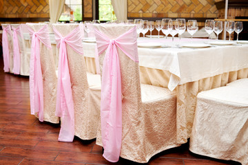 Fototapeta na wymiar Chairs with beige and pink cloth and table for guests served for banquet, copy space. Dinner table for wedding banquet in restaurant. Table setting