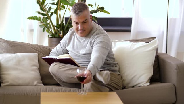 leisure and people concept - happy smiling man drinking red wine and reading book at home