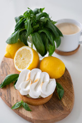 Lemon tartlets with basil on wooden desk and Cup of coffee on white table. Tasty treat on a light blue background.