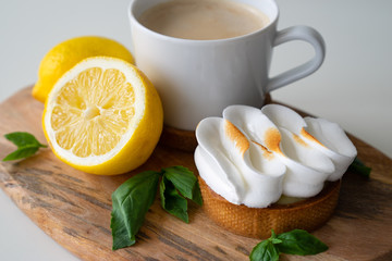 Lemon tartlets with basil on wooden desk and Cup of coffee on white table. Tasty treat on a light blue background.