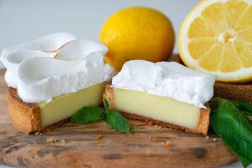 Lemon tartlets with basil on wooden desk and Cup of coffee on white table. Tasty treat on a light blue background.