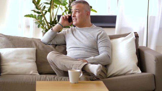 technology, people and communication concept - happy man calling on smartphone at home