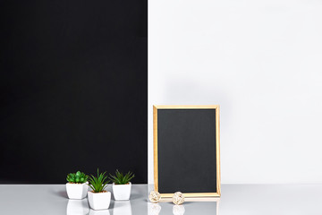 Wooden frame with black place for text. Mock up. Stylish room interior. Green plant in a white pot on black-white wall background