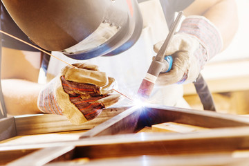 Male in face mask welds with argon-arc welding