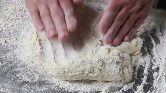 A male baker pats dough down to a uniform thickness