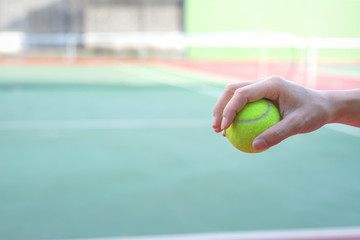 Hand holding tennis ball on court background