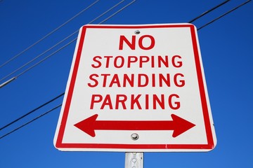 No Stopping Standing Parking Sign White Red Letters with Double-Arrows against Power Lines and...