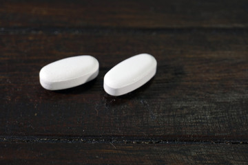 White Pharmaceutical medicine pills, tablets and capsules on a wooden background.