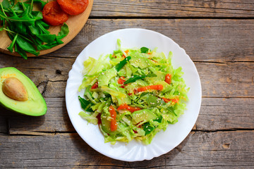 Healthy vegetarian avocado coleslaw. Home coleslaw salad with fresh avocado slices, dried apricots, arugula and sesame seeds on a plate and on a wooden table. Clean eating for beginners. Top view