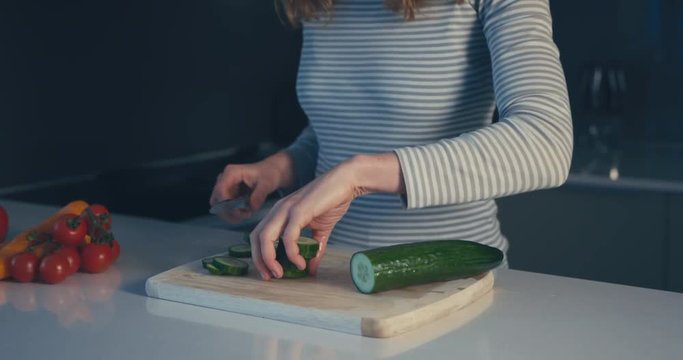 Young woman slicing cucumber in her kitchen