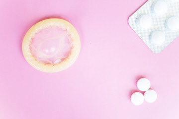 Condom and pills on pink background