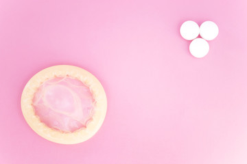 Condom and pills on pink background
