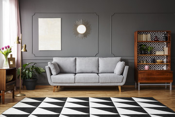 Black and white carpet with geometric pattern placed on the floor in dark living room interior with grey couch, vintage cupboard with books and wainscoting on the wall - obrazy, fototapety, plakaty