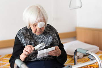 Visually impaired elderly 95 years old woman sitting at the bad trying to read her medical therapy...