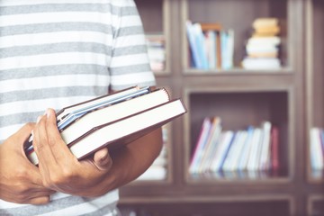 close up student young man hand holding books are placed front bookshelf in a library University. love to read education concept. with filter Tones retro vintage warm effect.