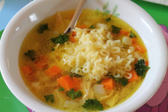 Fresh vegetable soup with alphabet pasta noodles. Silver spoon.