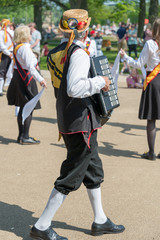 Morris dancer wearing straw hat plays accordion for the rest of the troupe on summers day in England
