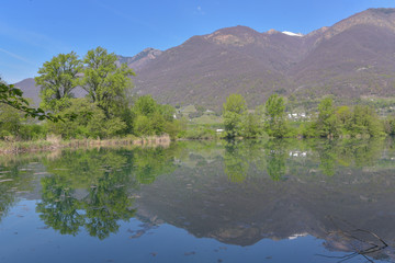 Panorama di un laghetto immerso nel verde con montagne che si riflettono sull'acqua