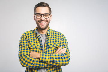 Happy young man. Portrait of handsome young man in casual shirt keeping arms crossed and smiling while standing against grey background