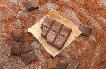 Crushed chocolate bar pieces and cocoa on gray background