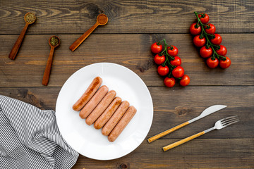 Grilled sausages on dark wooden table near cherry tomatoes and spices in wooden spoons top view