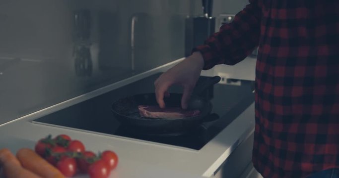 Young man cooking a steak in frying pan