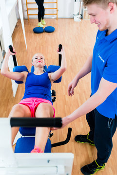 Female athlete and her physical therapist during exercise at workout equipment in health club
