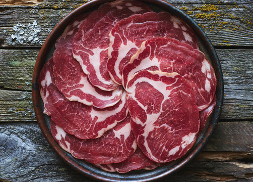 Delicious Italian meat coppa in plate on wooden rustic table top view 